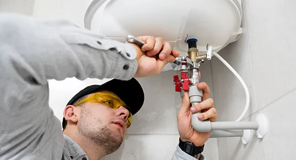 Professional plumber repairing sink pipes, wearing a yellow cap and safety glasses.