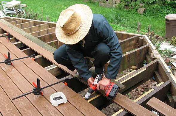 Worker in a straw hat installing a deck, highlighting professional deck installation services in Fort Mill, SC