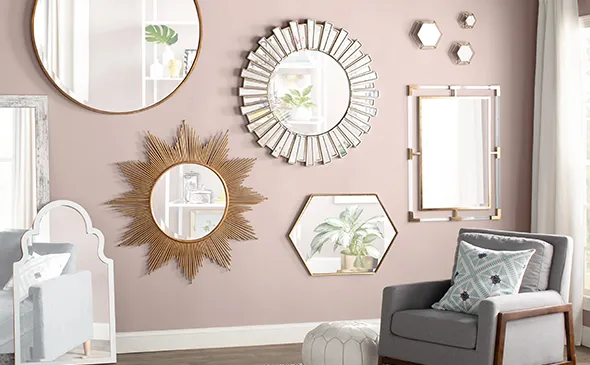 Elegant wall decorated with various stylish mirrors in different shapes—round, sunburst, and hexagonal—above a cozy armchair and a small table in a softly lit room.