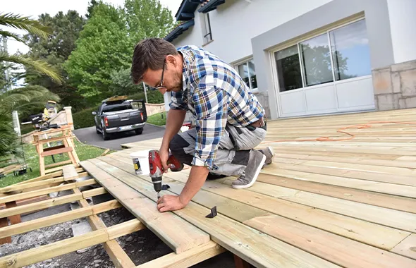 Worker in a straw hat installing a deck, highlighting professional deck installation services in Fort Mill, SC by Deck Assembly.