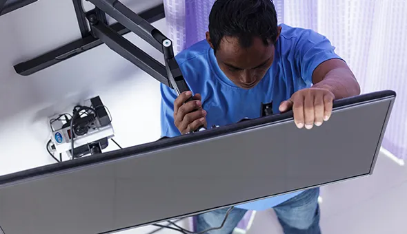 Technician adjusting a wall-mounted flat-screen TV using a full-motion mount, ensuring proper alignment.