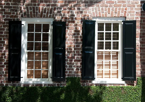 Brick exterior wall with two rustic windows secured with metal window grilles and black shutters in Lake Wylie, North Carolina.