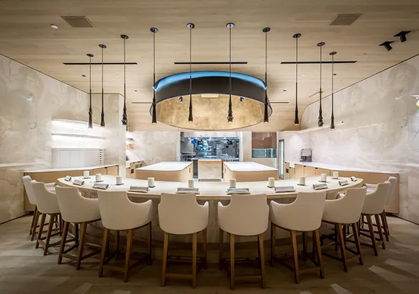 Elegant, spacious dining room with a large wooden table, white chairs, warm pendant lighting, and sophisticated stone accent wall behind the table.
