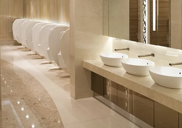 Clean, modern commercial restroom featuring a row of white urinals and two vessel sinks on a long beige countertop with large mirrors above