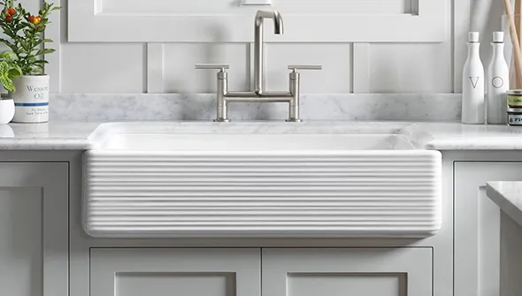 Close-up of a white farmhouse-style kitchen sink with a stainless steel faucet against a clean, bright background.